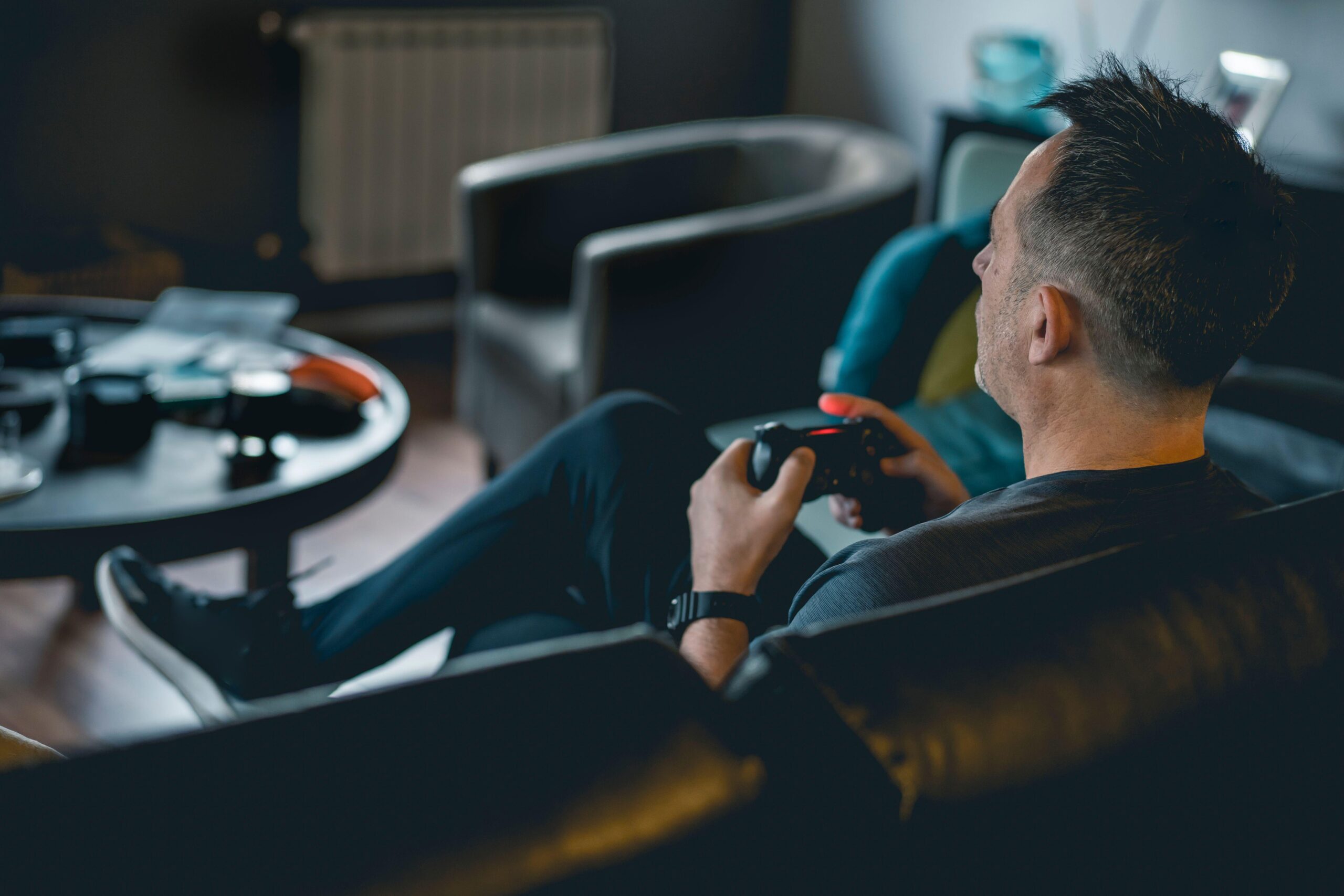An adult man sitting on a sofa and holding a joystick while playing Dying Light: The Beast on console