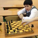 three children sitting in a classroom with two playing Chess