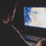 a man with headphones playing Mortal Shell 2 on his PC in a dark room