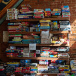board games stacked on shelves on brick wall to represent the newest addition of Everdell Silverfrost